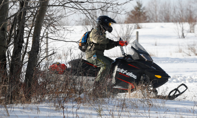 A man rides a snowmobile in the woods. 