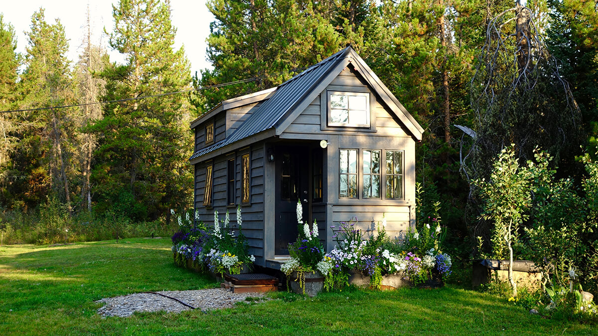 A tiny house in a country setting with beautiful flower beds around the house
