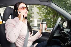 A woman talking on cell phone and drinking coffee while driving