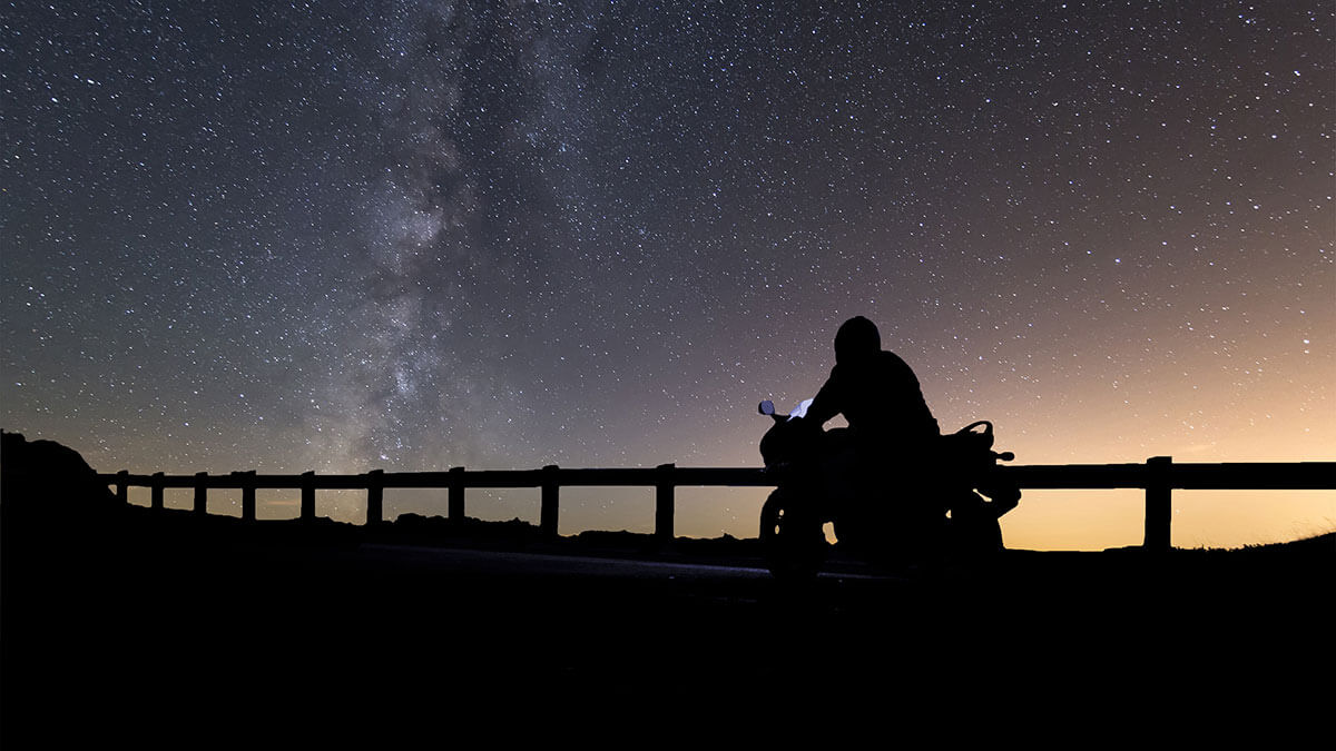 A motorcycle rider silhouetted against a starry night