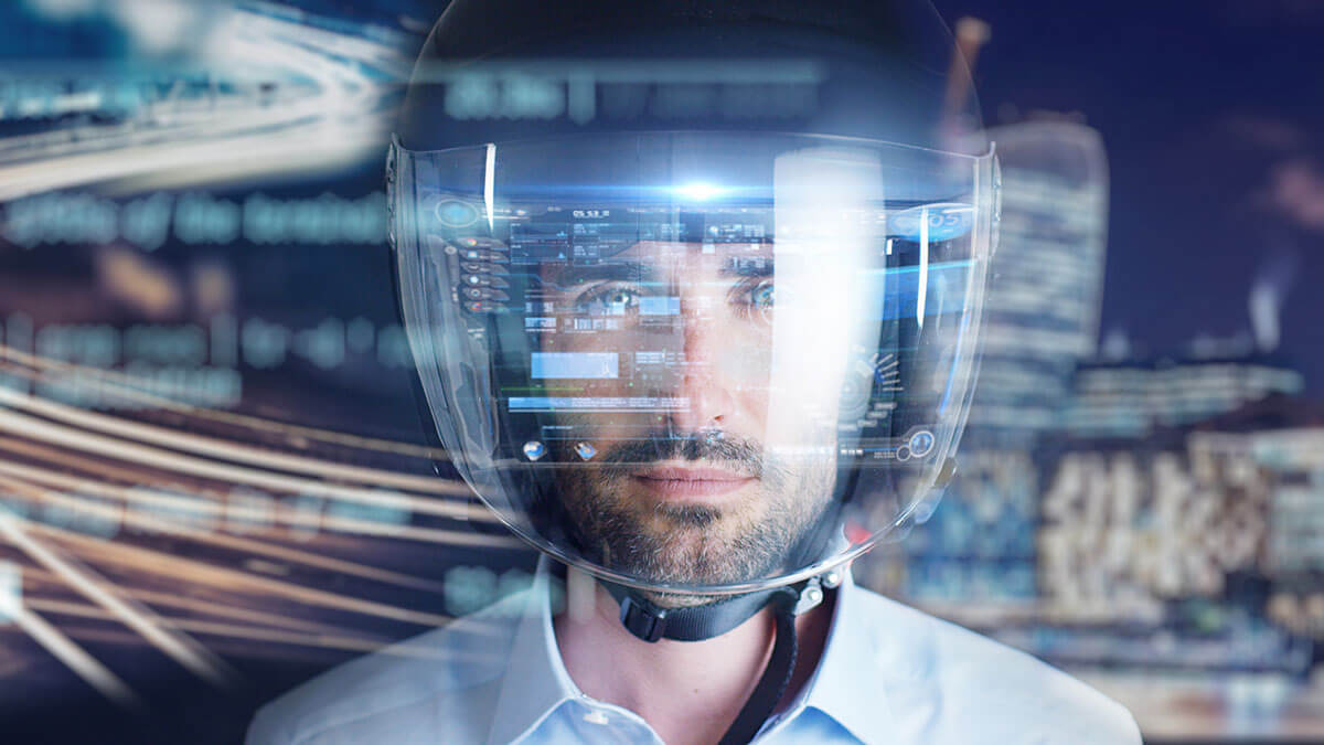 A close-up of a motorcycle rider wearing a helmet with technological images reflecting off of visor
